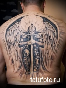 Фото тату на спине: ангел в доспехах с мечом и большими крыльями, выполненное в реалистичном стиле черными чернилами.