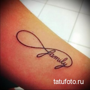 Фото тату на предплечье: знак бесконечности с надписью 'Family' внутри. Черно-серый рисунок татуировки, выполненный в каллиграфическом стиле.