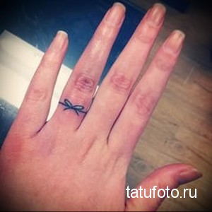 Небольшая татуировка в виде бантика на пальце руки. Деликатный дизайн, голубые чернила, женственный рисунок, минималистичный стиль.