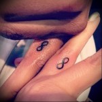Фото парных татуировок в виде символа бесконечности на пальцах двух людей. Минималистичный дизайн, черные линии, символ любви и связи.