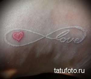 Фото тату бесконечности с маленьким красным сердцем и надписью 'love'. Белый рисунок на коже, символизирующий вечную любовь и страсть.
