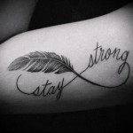 Фото тату бесконечность с пером и надписью 'Stay Strong' на предплечье. Черно-белый рисунок татуировки, выполненный в графичном стиле, с акцентом на детали пера.