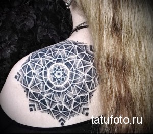 Фото татуировки на плече женщины, выполненной в технике дотворк. Изображена сложная геометрическая мандала с множеством мелких точек.