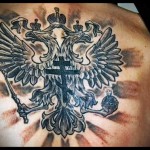 Фото тату на лопатке: Большой двуглавый орел, реалистичный рисунок, черно-серые тона, лучи света, патриотическая татуировка.