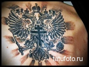 Фото тату на лопатке: Большой двуглавый орел, реалистичный рисунок, черно-серые тона, лучи света, патриотическая татуировка.