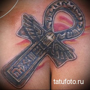 Фото тату сочетания древнеегипетского символа Анкха и христианского креста на груди мужчины. Черно-серый рисунок татуировки с иероглифами.