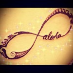Фото тату бесконечности с надписью 'aloha' на коже. Коричневый рисунок, выполненный тонкими линиями и украшенный узорами.