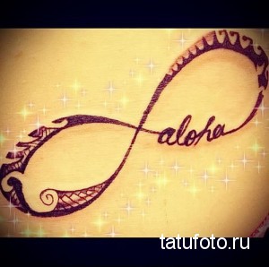 Фото тату бесконечности с надписью 'aloha' на коже. Коричневый рисунок, выполненный тонкими линиями и украшенный узорами.