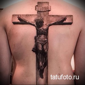 Фото тату распятия Иисуса Христа на спине мужчины. Детализированный рисунок в реалистичном стиле, выполненный в черно-серых тонах.
