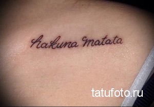 Фото тату надписи 'Hakuna Matata' выполненной коричневым цветом на ключице. Простой и лаконичный рисунок татуировки, популярный среди поклонников мультфильма 'Король Лев'.