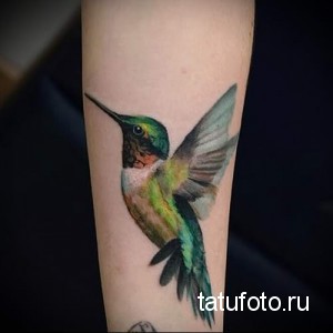 Фото акварельной татуировки колибри на предплечье. Татуировка выполнена в ярких, насыщенных цветах с эффектом размытия.