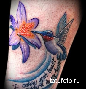 Фото тату колибри, парящей над цветком ириса. Татуировка выполнена в ярких цветах с использованием плавных переходов и теней.