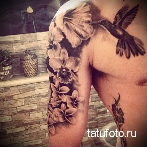 Фото тату: черно-белая татуировка с изображением колибри, парящего над цветами, на плече и груди. Детализированный рисунок в стиле графика.