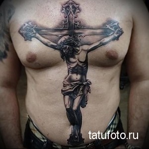 Фото тату распятия Иисуса Христа на груди мужчины. Детализированный рисунок в реалистичном стиле, выполненный в черно-серых тонах.