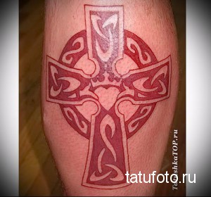 Фото татуировки кельтского креста на ноге. Красный рисунок с белыми контурами, выполненный в традиционном стиле.