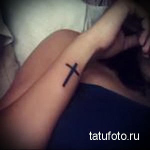 Фото тату: Маленький черный крест на запястье девушки. Простой и элегантный рисунок татуировки, выполненный в минималистичном стиле.