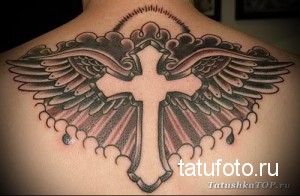 Фото татуировки креста с крыльями на спине мужчины. Детализированный рисунок тату, выполненный в черно-серых тонах.