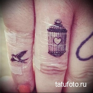 Фото тату клетки с птицей и сердцем на пальцах. Черно-белая татуировка, выполненная тонкими линиями. Нежный и символичный эскиз тату.