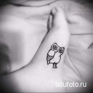 Фотография миниатюрной татуировки совы на лодыжке. Татуировка выполнена в черном цвете с использованием тонких линий.