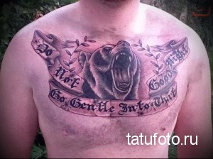 Фото тату на груди с изображением рычащего медведя и цитаты "Do Not Go Gentle Into That Good Night". Черно-серые тона, реалистичный стиль.