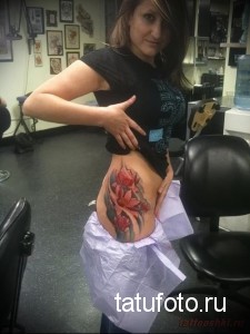 Фото татуировки с изображением нескольких красных лотосов на боку. Детализированный рисунок с использованием ярких цветов и теней.