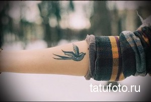 Фото тату: небольшая акварельная татуировка с изображением летящей ласточки на внутренней стороне запястья.