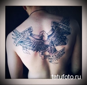 Фото татуировки орла с лентой с надписью "Freedom Through Strength" на спине. Чёрно-серый рисунок, реалистичный стиль, детализированные перья и мощные крылья.