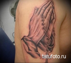 Фото тату: Черно-белая татуировка молящихся рук с четками и крестом на плече. Детализированный и реалистичный рисунок татуировки.