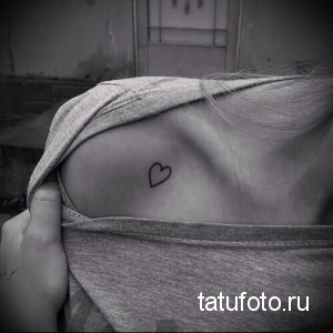 Фотография небольшой татуировки в виде сердца, расположенной на ключице. Рисунок выполнен тонкими черными линиями.