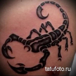 Фото черной татуировки скорпиона на плече. Рисунок выполнен в графическом стиле с использованием четких линий и контрастных теней. Подходит для любителей темных татуировок.