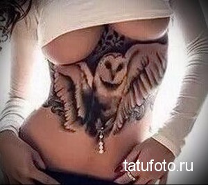 Фото татуировки совы, выполненной в реалистичном стиле на боку. Детализированное изображение с акцентом на перья и взгляд.