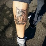 Фото татуировки совы с часами, выполненной в стиле blackwork на ноге. Контрастные линии и геометрические элементы.
