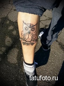 Фото татуировки совы с часами, выполненной в стиле blackwork на ноге. Контрастные линии и геометрические элементы.