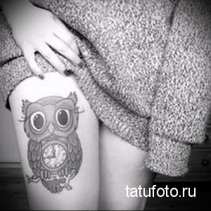 Фото тату совы с часами на бедре. Черно-белый рисунок, мультяшный стиль, большие глаза.