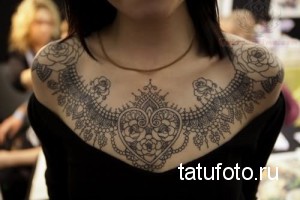 Фотография женской татуировки, выполненной в стиле кружева, покрывающей плечи и верхнюю часть груди. Рисунок выполнен в черном цвете.