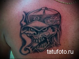 Фото тату черепа в бейсболке Dodgers на груди. Черно-серый рисунок с детальной проработкой и дымом от сигары.