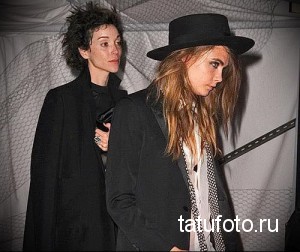 Фото с тату-конвенции: две стильные девушки в темной одежде, одна в шляпе, демонстрируют свои татуировки.
