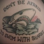 Фото тату: татуировка акулы с надписью "Don't be afraid to swim with sharks" на боку. Мотивационный рисунок татуировки в стиле олд скул.