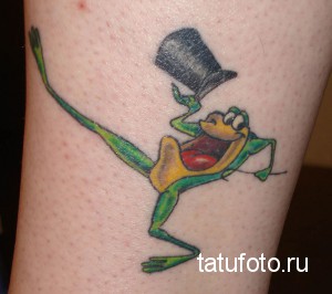 Фото тату лягушки на руке. Зеленая лягушка в цилиндре и с бабочкой, забавная и мультяшная татуировка.