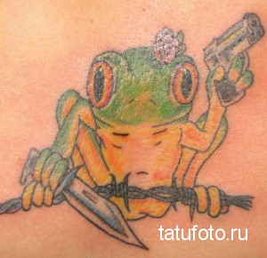 Фото татуировки с изображением зеленой лягушки с пистолетом и ножом, выполненной в мультяшном стиле с элементами олдскул.