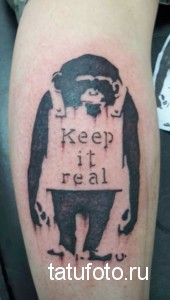 Фото тату на руке: силуэт обезьяны с надписью 'Keep it real', выполненное в технике трайбл с использованием черного цвета.