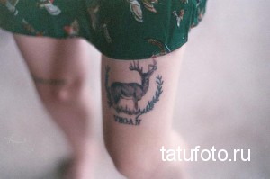 Фото минималистичной татуировки оленя на ноге. Рисунок выполнен в черном цвете с добавлением надписи 'VEGAN'. Простой и лаконичный дизайн.