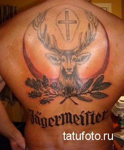 Фотография татуировки оленя на спине, с изображением креста и логотипа Jägermeister. Рисунок выполнен в черно-белых тонах.