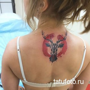 Фото тату оленя в геометрическом стиле на спине. Черно-белая татуировка, треугольники, красный круг, современный дизайн.