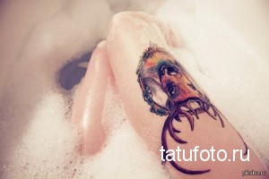 Фото акварельной татуировки головы оленя на стопе, словно парящей в пене. Рисунок выполнен в мягких, размытых тонах.