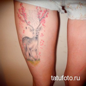 Фото нежной татуировки оленя на бедре, окруженного цветущей сакурой. Рисунок выполнен в акварельной технике с использованием пастельных тонов.