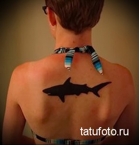 Фото простой татуировки в виде силуэта акулы на спине. Черно-белое изображение, минималистичный дизайн.