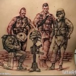 Фото тату на спине с изображением группы солдат у мемориала с оружием и шлемами. Реалистичный стиль, черно-серые тона.