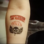 Фото тату черепа в парашюте с надписью 'Brothers in Arms'. Рисунок выполнен в коричневых тонах.