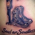 Фото тату на плече: ботинок, кинжал и надпись 'Soul or Soulless'. Черно-серый рисунок татуировки в реалистичном стиле.